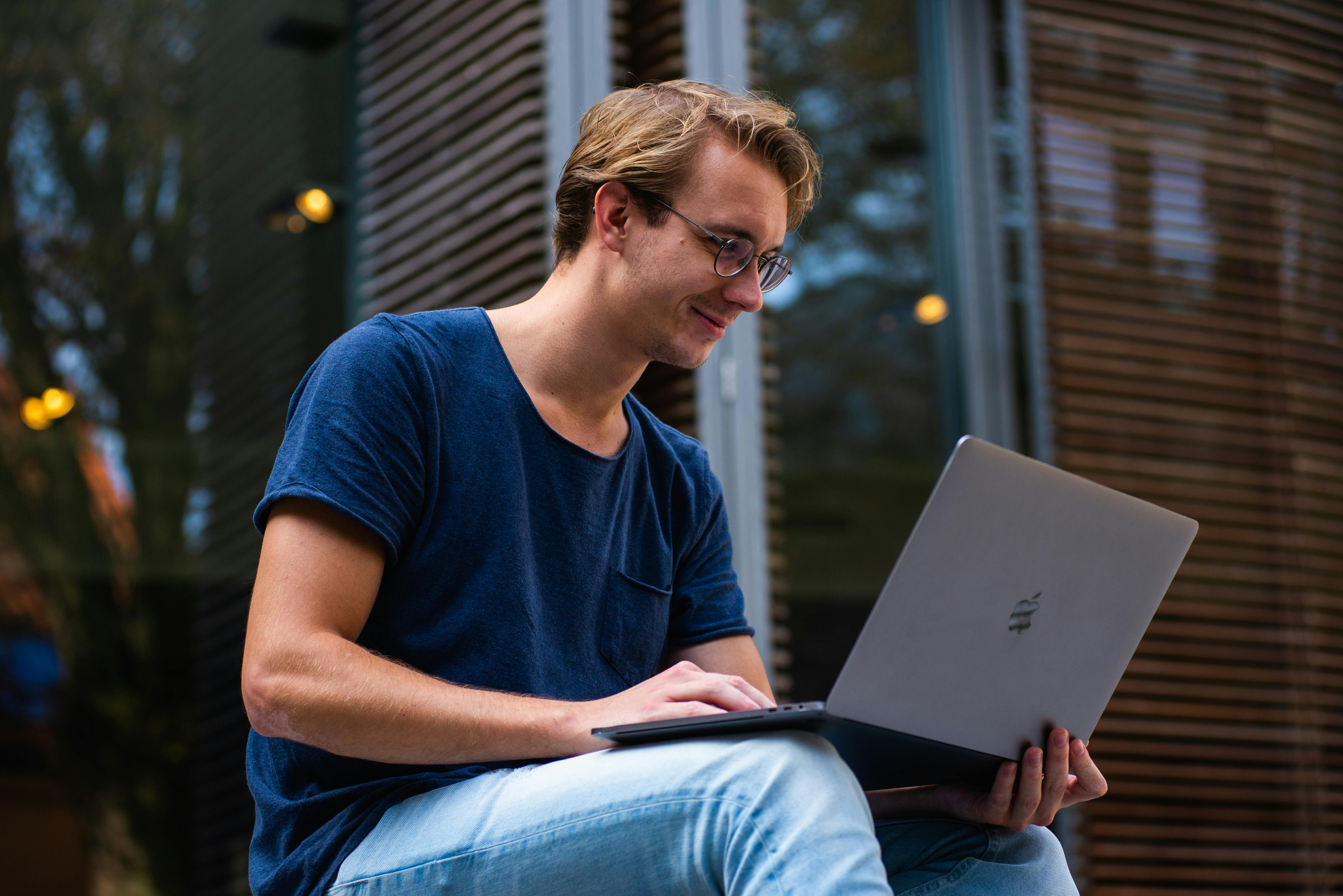 Young man using his laptop outside of his house. Practicing smart habits to keep his financial accounts safe.