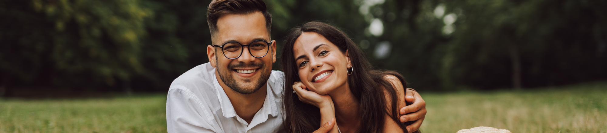 young Caucasian couple laying in open field smiling at camera