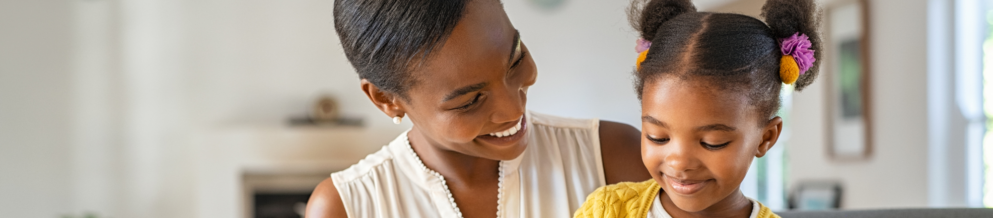 Black mother and daughter sitting on couch smiling