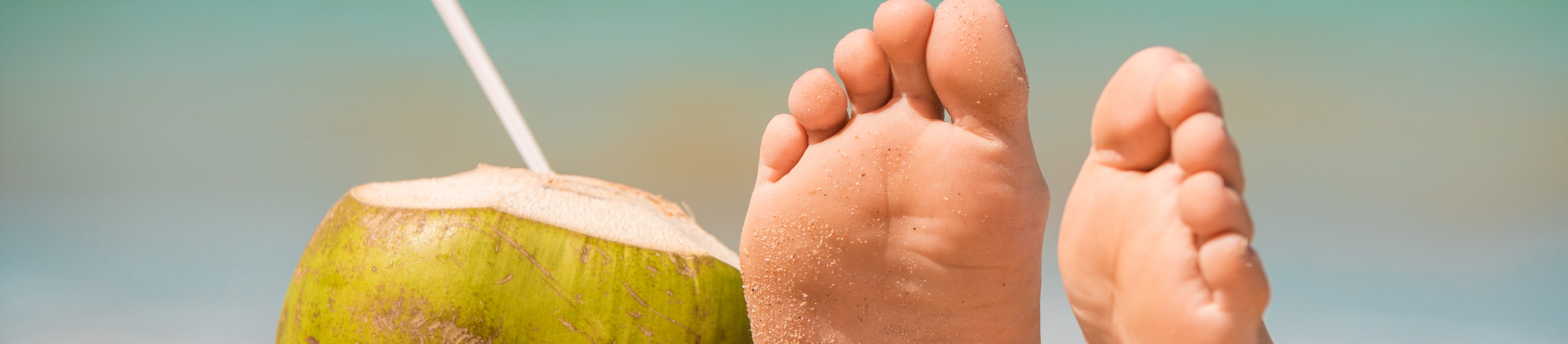 Feet by coconut drink in sand on beach